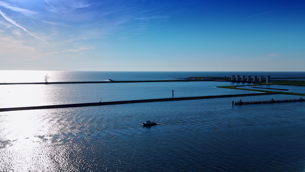 Motor boat slowly moves by the waterscape of the Markermeer Lake on sunny day. Long dams and sluices on the dike at backdrop. Aerial view. Lelystad, the Netherlands.