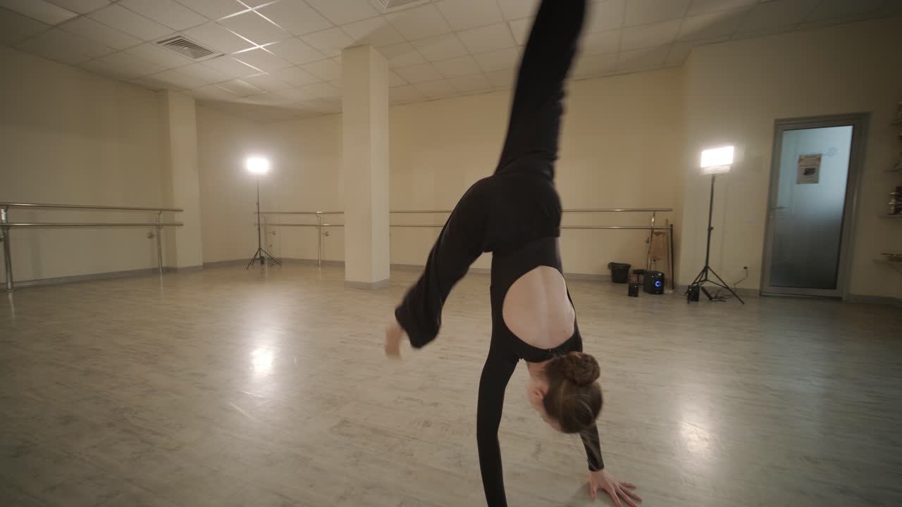 검은색 댄스웨어를 입은 젊은 발레 학생들이 나무 바닥과 벽에 장착된 바를 가진 넓은 발레 스튜디오에서 자세를 연습하는 그룹.