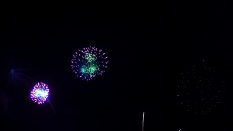 fuegos artificiales morados y rosas con centros verdes explotan en lluvias de luz