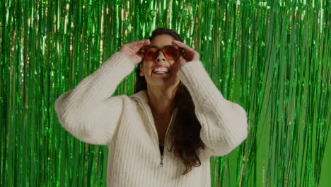 woman celebrating st patrick's day standing in front of green tinsel curtain wearing prop shamrock deely boppers and glasses