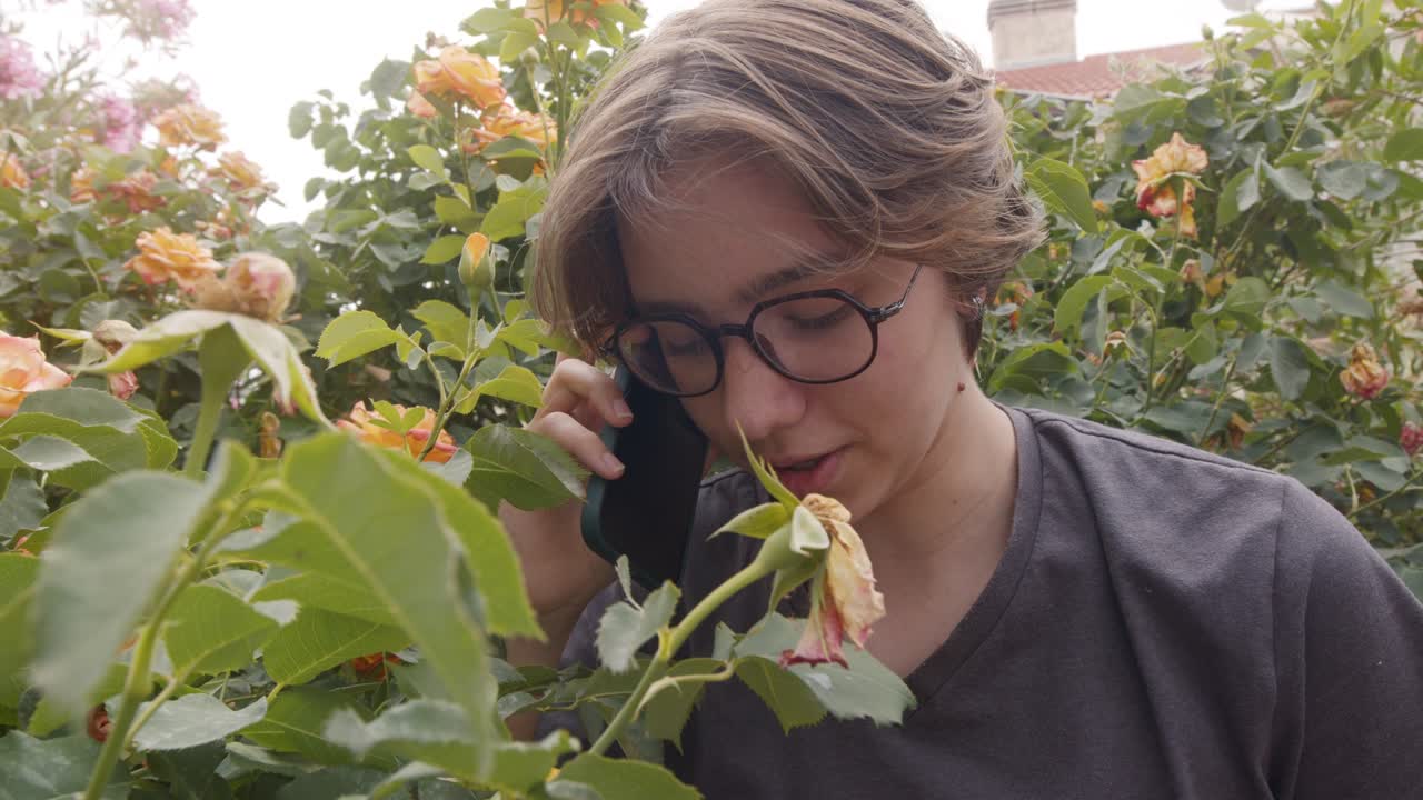 젊은 소녀는 자연에서 꽃 근처에 드폰으로 이야기하고 있습니다.