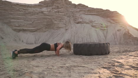 girl on sand quarry jumping burpee with push-ups through the wheel in the sand