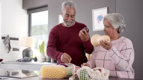 Pareja-Birracial-De-Alto-Nivel-Desempacando-Comestibles-En-La-Cocina,-Inalterada,-En-Cámara-Lenta