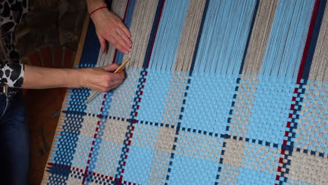 woman working on blue and beige weaving project, panning shot