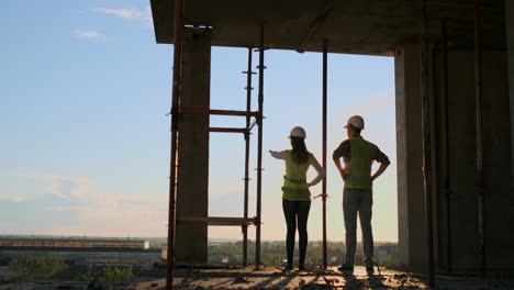 negocio de construcción: concepto de trabajo en equipo: joven ingeniero de pie detrás mirando un sitio de construcción con un casco de seguridad