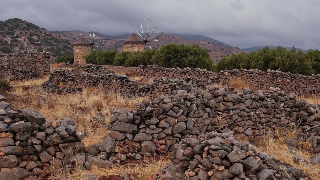 Mulini a vento e muri storici in pietra in un paesaggio montano arido