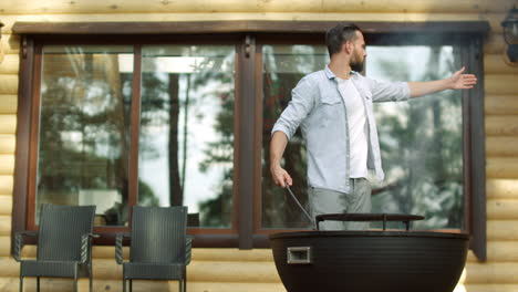 Serious-guy-using-poker-outdoors.-Handsome-man-putting-firewood-in-grill.