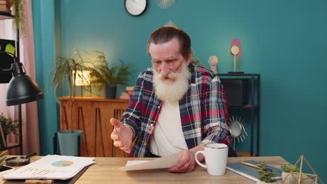 shocked senior man analyzing paperwork graphs charts calculating monthly expenses bank bills