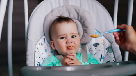 baby feeding from spoon. mother's hand gives the orange stuff to her son and he makes faces after.