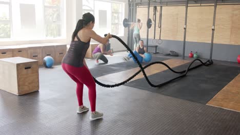 focused unaltered biracial woman exercising with battling ropes at gym, in slow motion