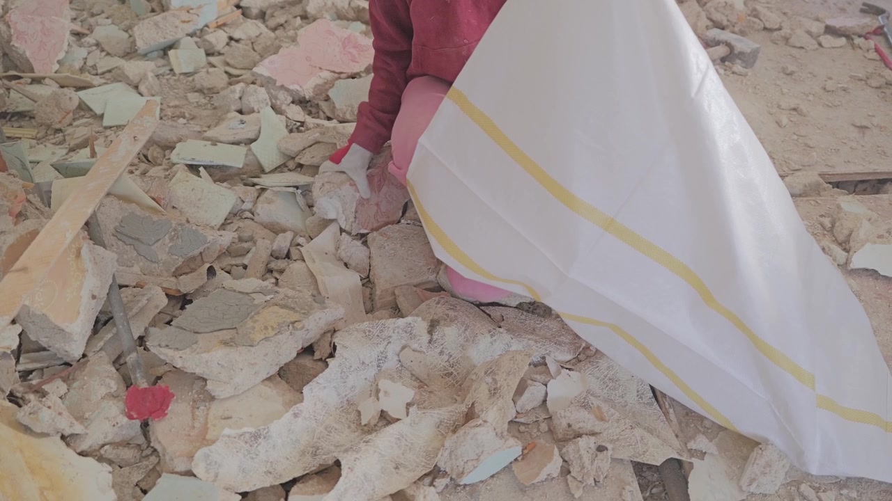 Protected worker gathering broken plaster into heavy duty waste sack