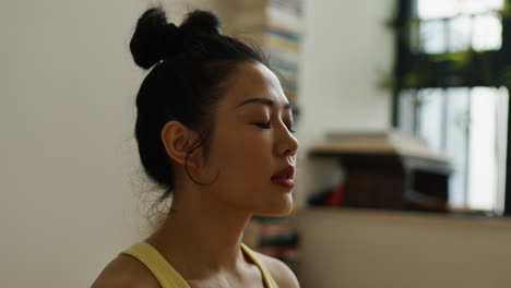 young asian woman meditate alone in her house, close up of female focusing on breath and sharpening the mind in full concentration practice portrait