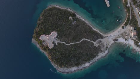 Aerial-top-down-shot-of-triangular-Porto-Palermo-castle,-situated-in-the-bay-of-Porto-Palermo-with-blue-ocean-surrounded-by