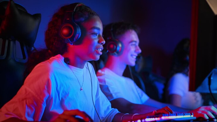 White boy and black girl teens in headsets playing video games in video game club with blue and red illumination, talking in voice chat and giving each other five. Slow motion