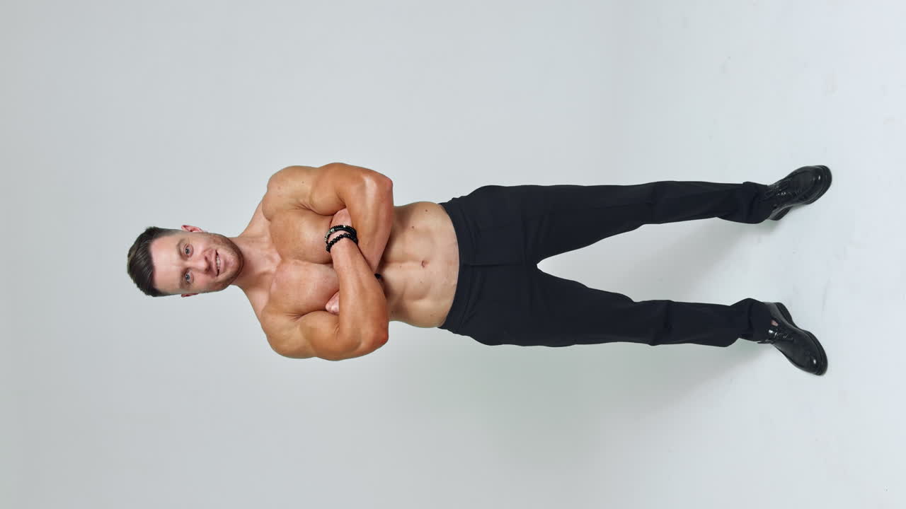 Caucasian man with athletic body stands isolated. Sportsman in black trousers posing in front of camera. Vertical screen.