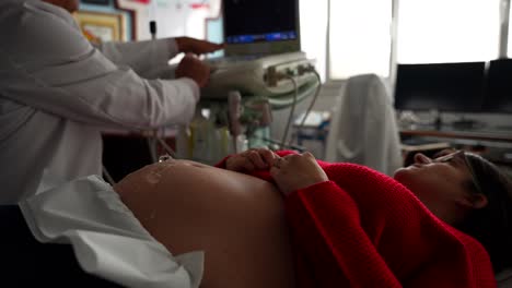 gynecologist adjusting the ultrasound machine while pregnant patient waits