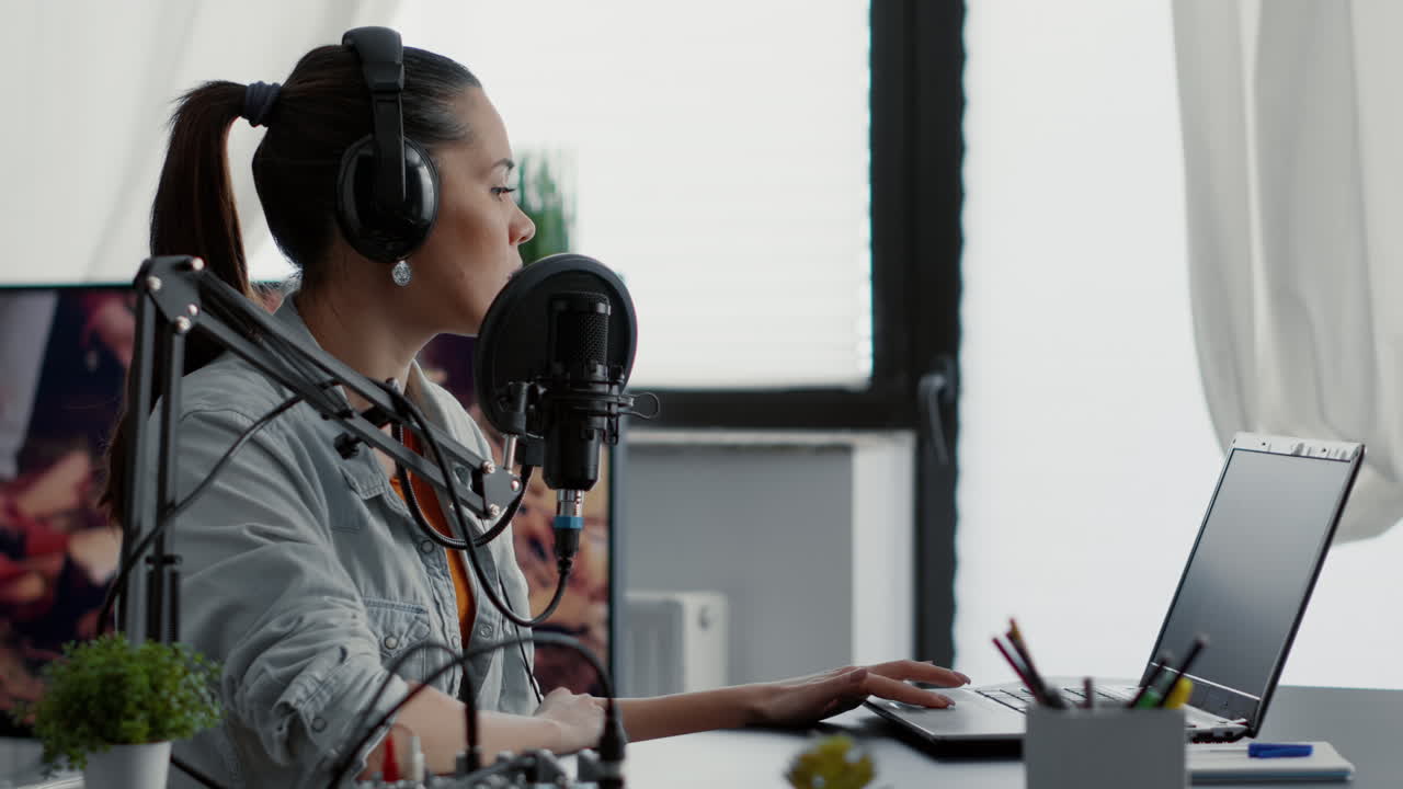 Internet radio show host talking on microphone while checking subject list on laptop