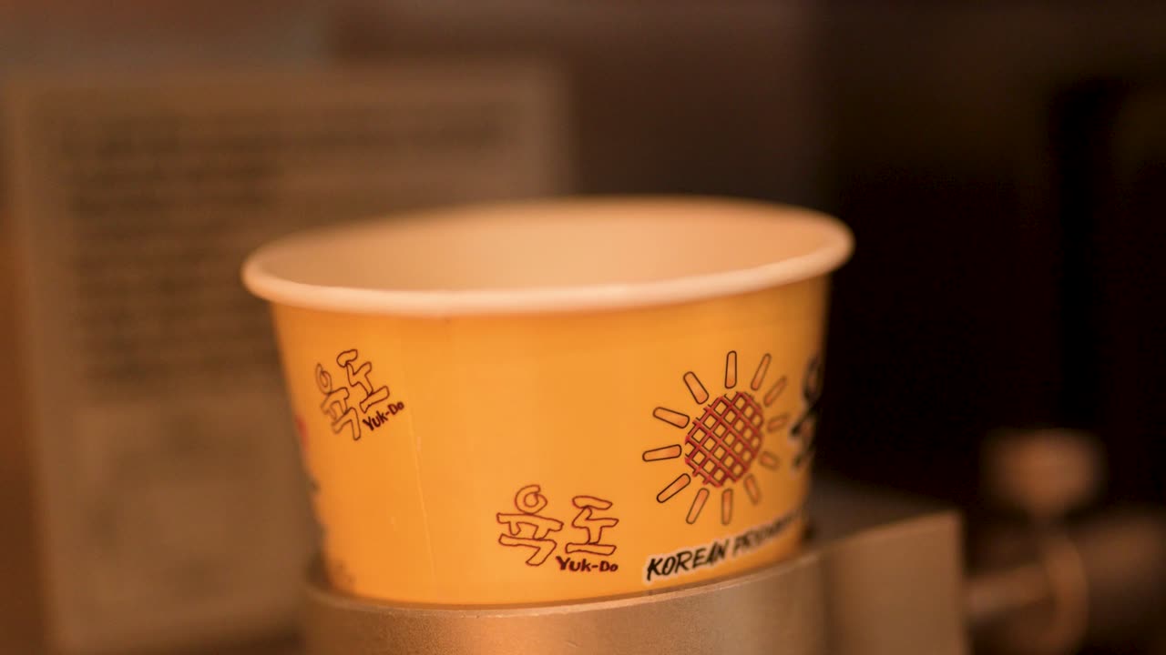 Close-up shot of vanilla soft serve ice cream filling a yellow paper cup from machine