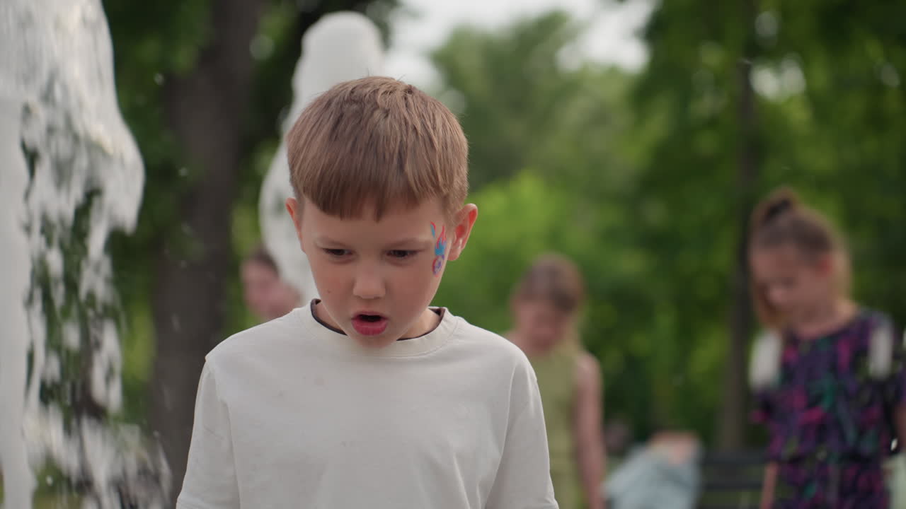 cheerful young kid and other children playing near water fountain in park, turning to run from splash, summer sunlight on droplets, laughter and curiosity filling green outdoor space