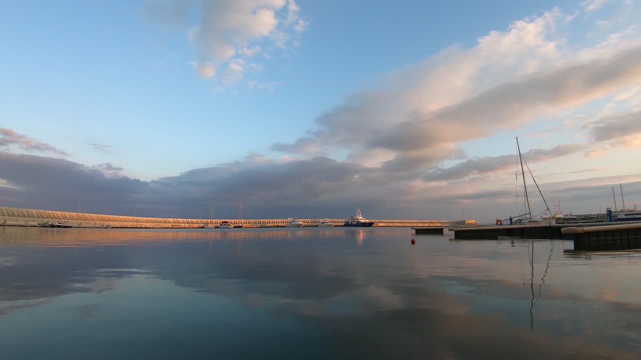 Time lapse of fishing port at sunset. Ships, boats and pontoons in the seawater. People walking.  Beautiful colors and reflection on the water. White clouds in the sky. Sarafovo Dockland, Bulgaria.