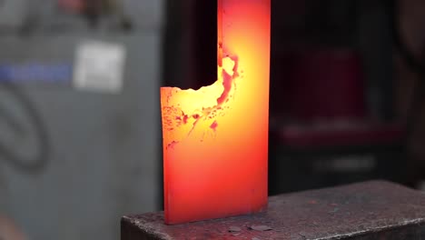 blacksmiths forging hot metal with hammer in workshop