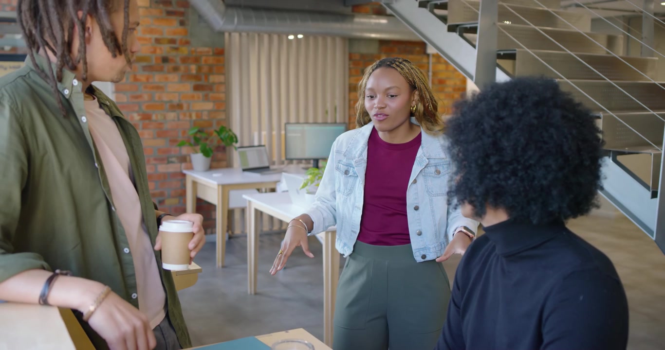 Equipe afro-americana discutindo no escritório, mulher se aproximando de homem sentado e gesticulando para o laptop.
