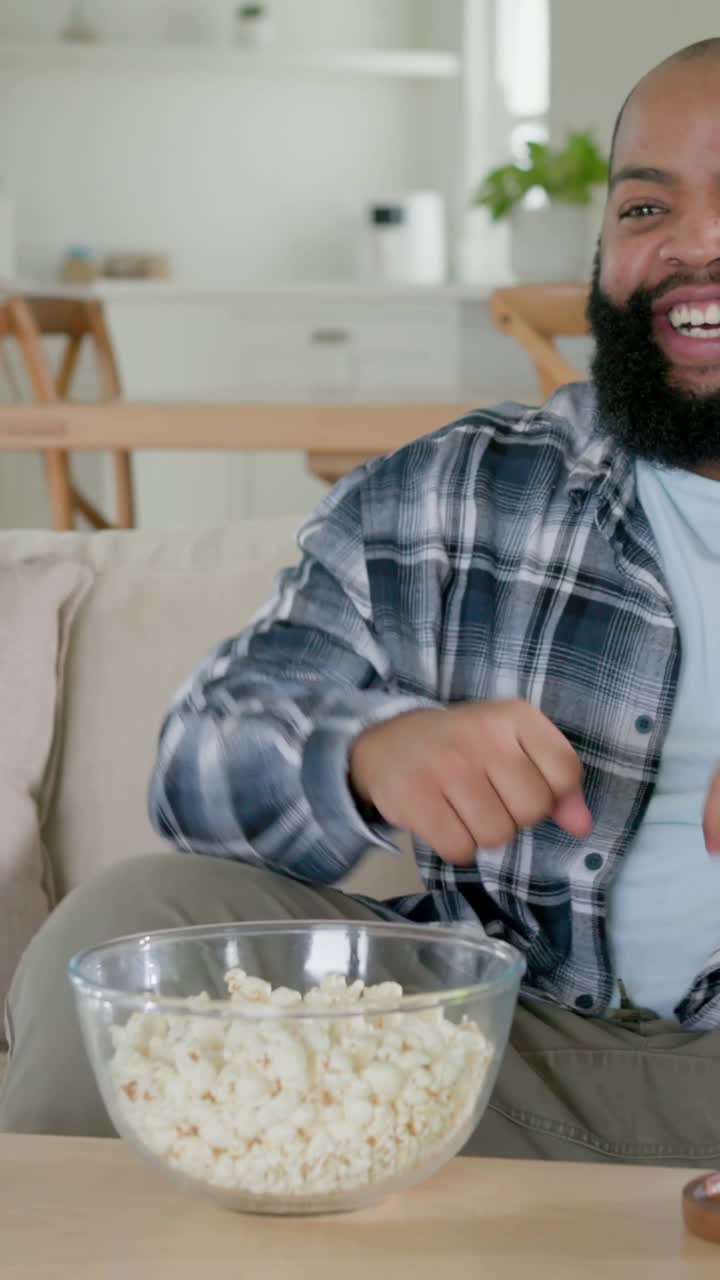Vertikal video: Klappende mand i ternet skjorte efter tv-mål på sofaen, holder øl, popcorn med bold i nærheden
