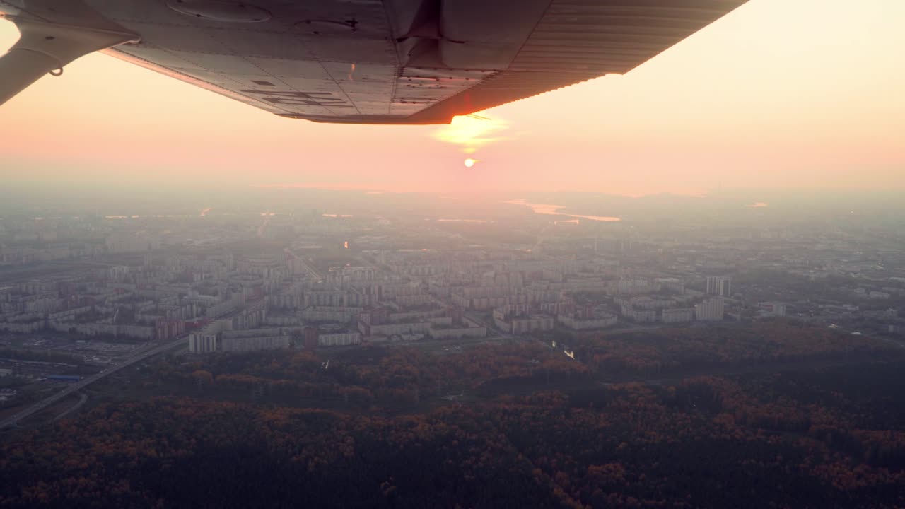 A propeller plane is flying above a village or a small town during a sunset and golden hour, beautiful landscape and nice weather, passenger point of view, smooth shot, cinematic shot
