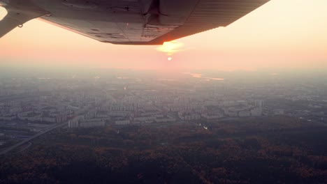 a propeller plane is flying above a village or a small town during a sunset and golden hour, beautiful landscape and nice weather, passenger point of view, smooth shot, cinematic shot