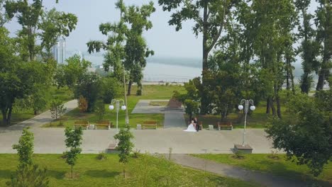 newlywed-couple-rests-on-bench-in-green-park-upper-view