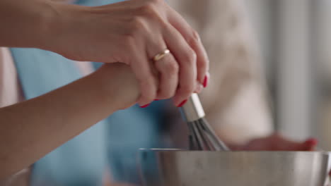 mother and daughter are cooking in home closeup of hands of woman and little girl mixing dough by whisk