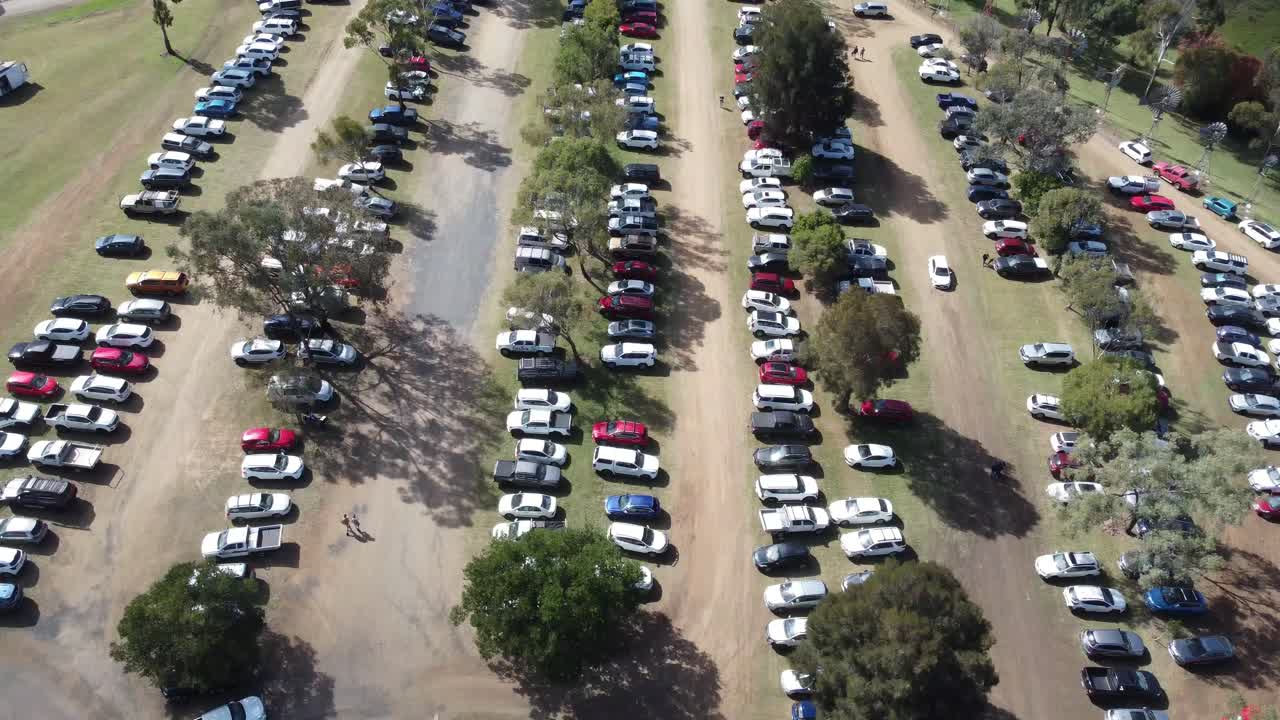 4K video of a drone ascending over an unpaved carpark full of parked cars then showing large private properties in a regional town in Australia