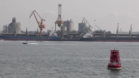 A-buoy-floating-in-the-sea-water-with-the-construction-site-on-the-coastal-line-under-the-gloomy-sky