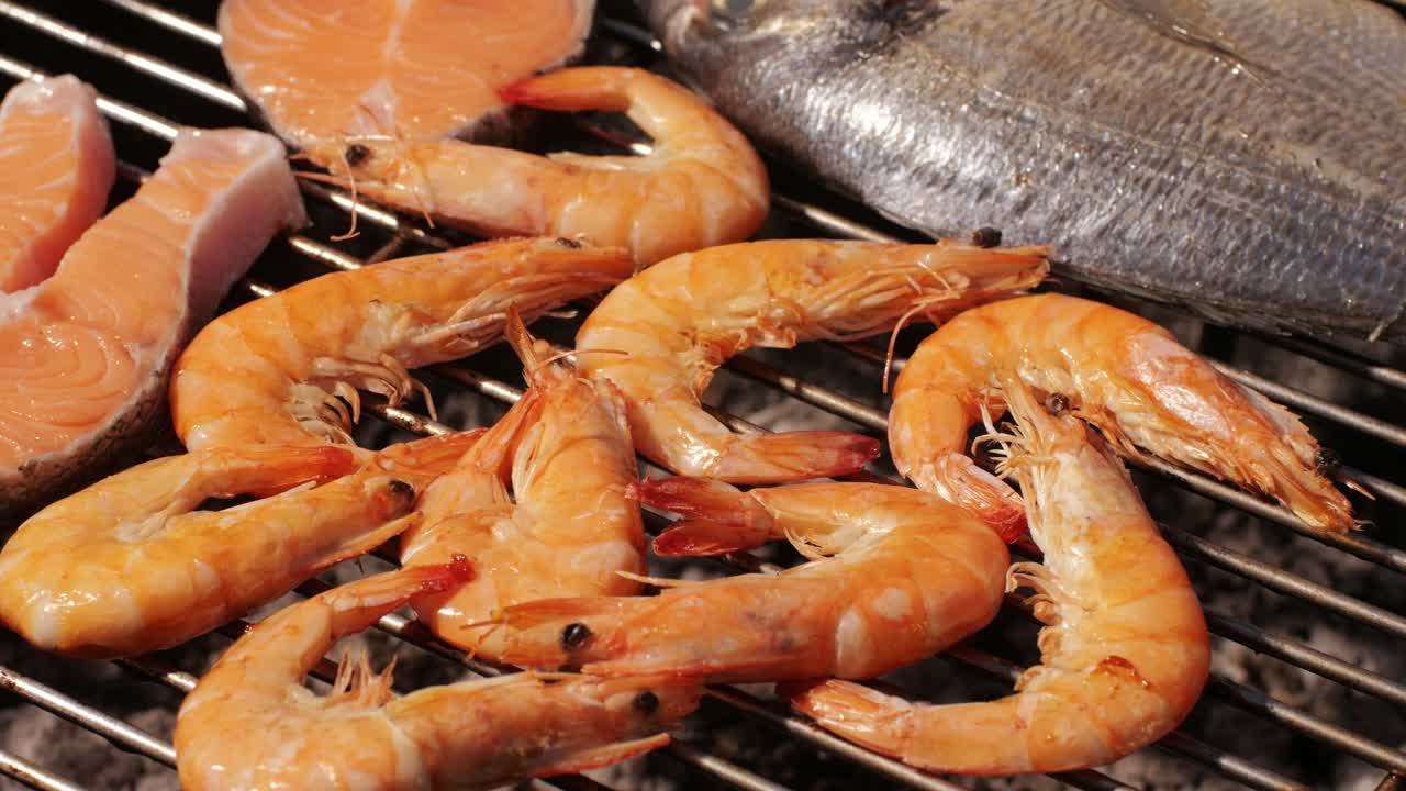 Chef cooking shrimps with oil and spices on grill close-up. Prawns on fire throwing them on pan. Dorado and salmon fish steak on frying grill. Restaurant Food concept. Sea food barbecue.