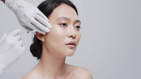 회색 바탕에 있는 아시아 여성의  ⁇ 에 주사를 주입하는 장갑을 입은 손, 슬로우 모션