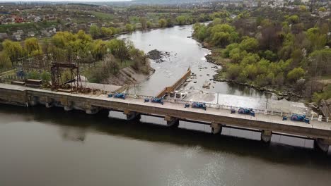 A huge construction with a bridge stands on the river outside the city for water purification on the background of wonderful landscape of green trees and with buildings. Close-up. Aerial view.