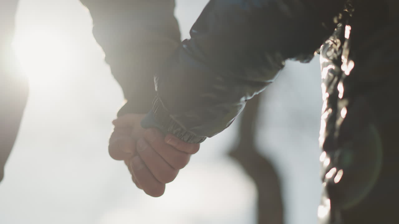 손을 잡고 있는 성인과 아이의 클로즈업, 손에서 반사되는 빛, 아이는 검은색 재을 입고 있다