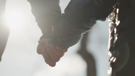 a close-up of an adult and child holding hands, with sunlight reflecting off their hands, the child is wearing a black jacket