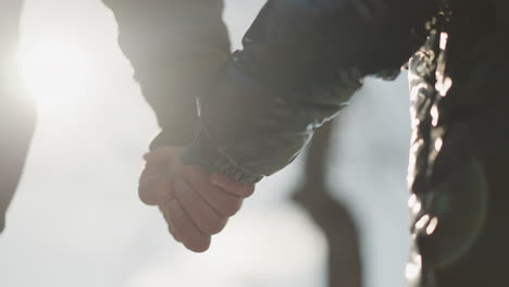 un primer plano de un adulto y un niño tomados de la mano, con la luz del sol reflejada en sus manos, el niño lleva una chaqueta negra