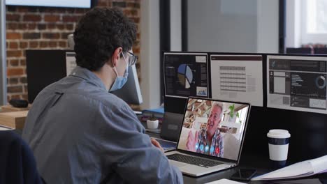 Caucasian-man-on-laptop-video-chat-wearing-face-mask-in-office