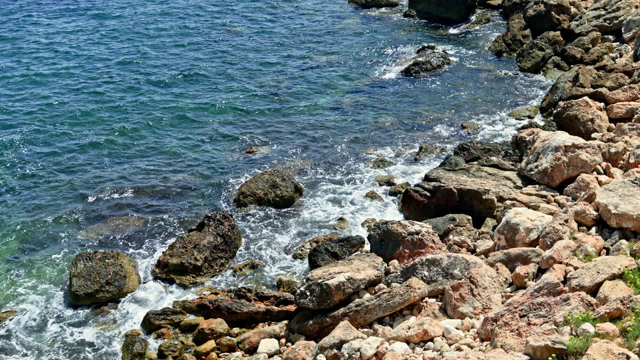 L'oceano con acqua cristallina infrange le onde contro scogliere rocciose. Costa con montagne rocciose. L'acqua di mare forma schiuma colpendo le rocce
