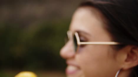 Joyful-brunette-sensual-girl-licking-ice-cream-on-a-cone---white-and-yellow-scoops.-While-looking-into-camera-and-smiling.-Captured-in-side-view.-Green-outdoors.-Close-up