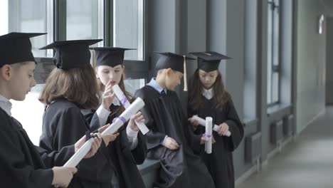 group of happy multiracial preschool students in mortarboard and gown. they are talking and holding diplomas.