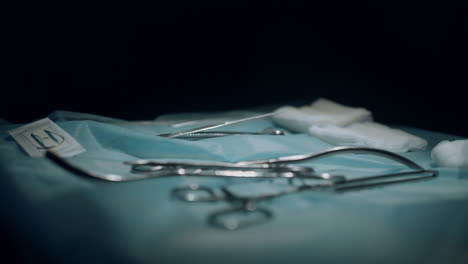 Table-with-surgical-instruments-in-dark-sterile-operating-room-side-view-closeup