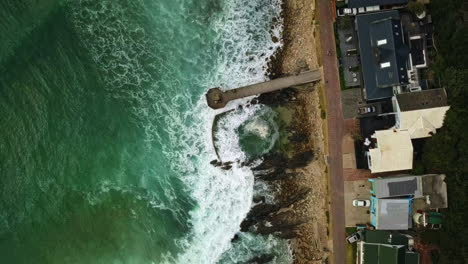 aerial cenital shot of a beach with great waves, a wooden pier and some houses on the beach