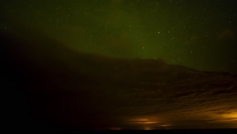 beautiful time lapse of green northern lights above dark clouds with a starry night sky with shooting stars