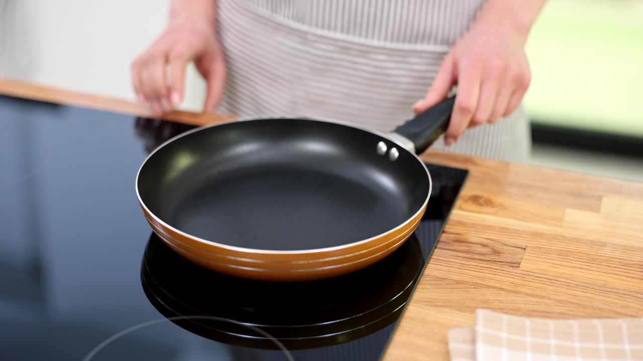 Person holding an empty frying pan over an induction cooktop in a kitchen