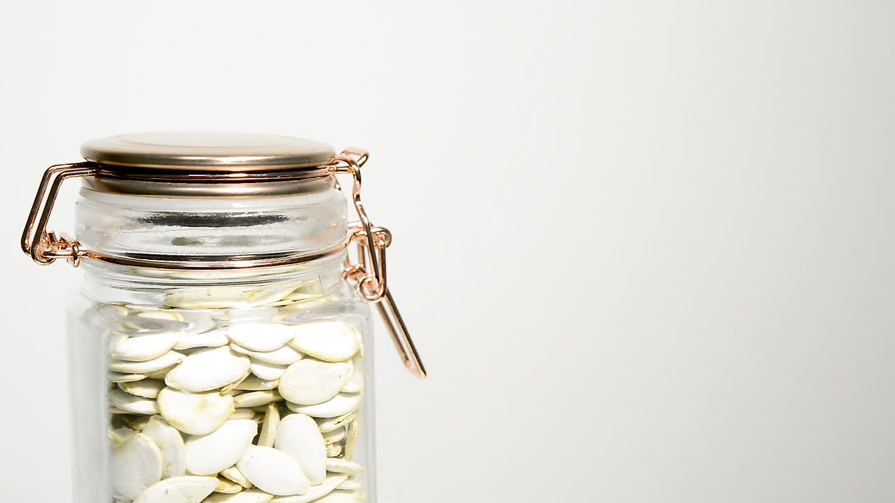 흰색 스튜디오 배경에서 회전하는 원시 호박 씨앗으로 가득 찬 유리 메이슨 항아리