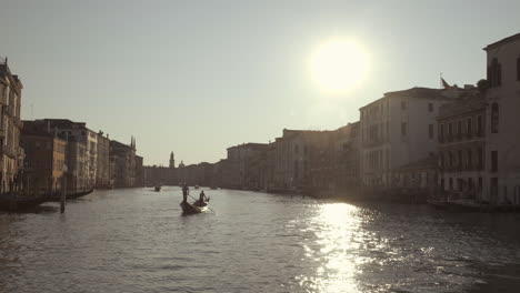 gondola sailing in canal grande lit by warm sunrise with water reflections, venice, italy