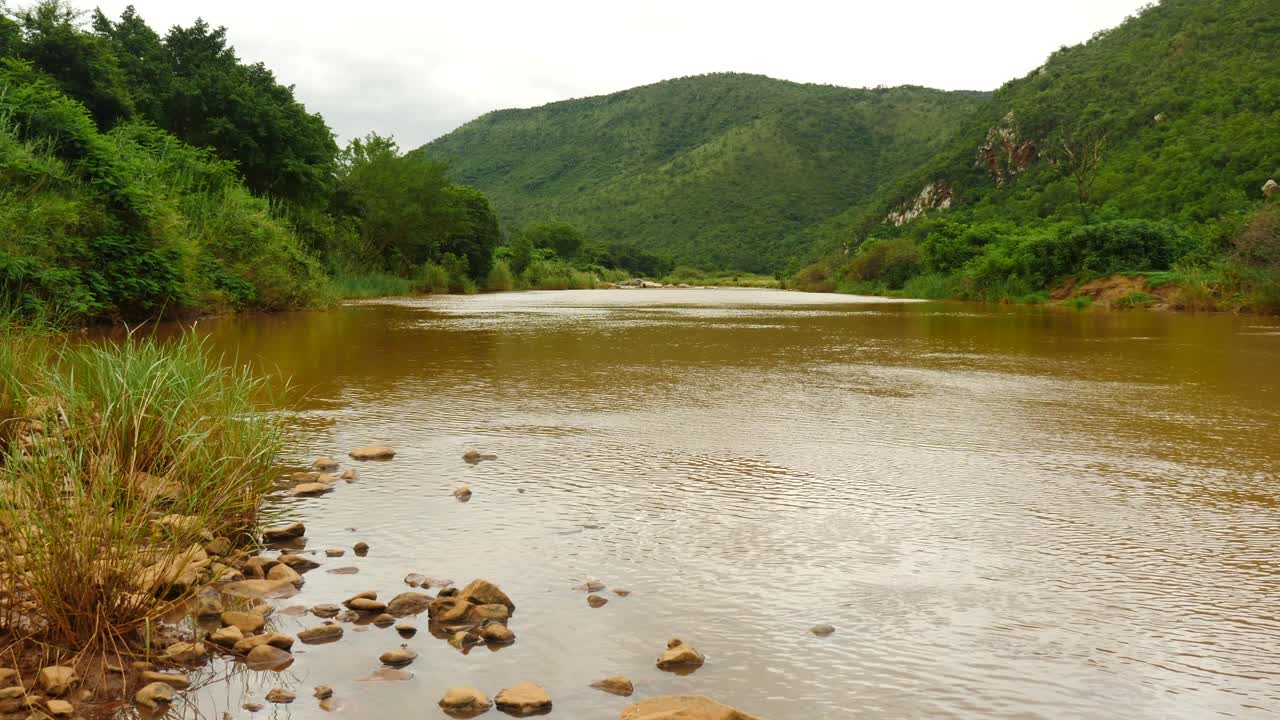 río pongola fangoso que fluye hacia la cámara, a través del paisaje montañoso africano en verano, pan de hierba al agua